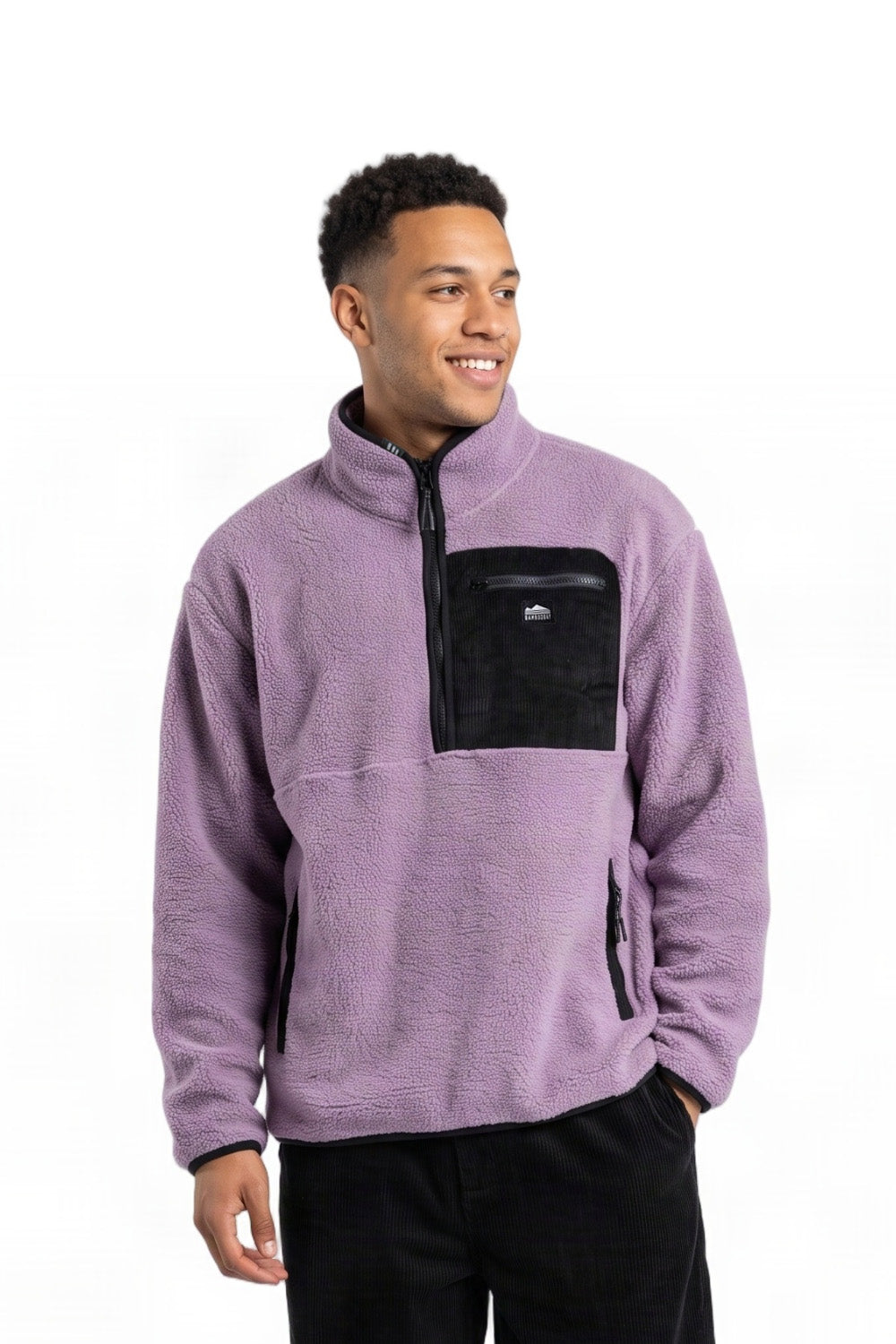 A man wearing a light purple fleece pullover with a black chest pocket and black zipper details, paired with black pants, against a plain white background.