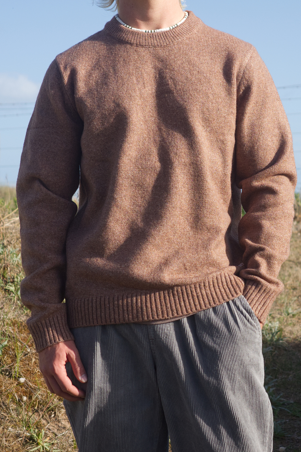 Model wearing a light brown knitted jumper and grey cord trousers.